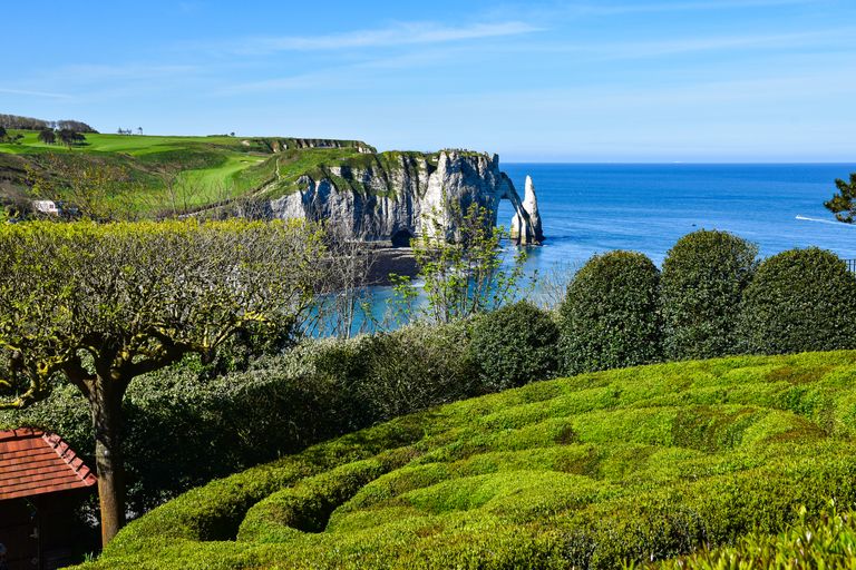 Beautiful landscape of Etretat cliffs, greenery, and blue sea under a clear summer sky in Normandy, France.